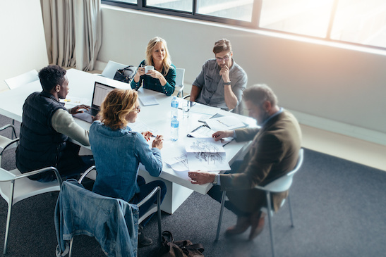 Business people working and discussing together in meeting at office. Businessman looking at building sketch with colleagues sitting around table.